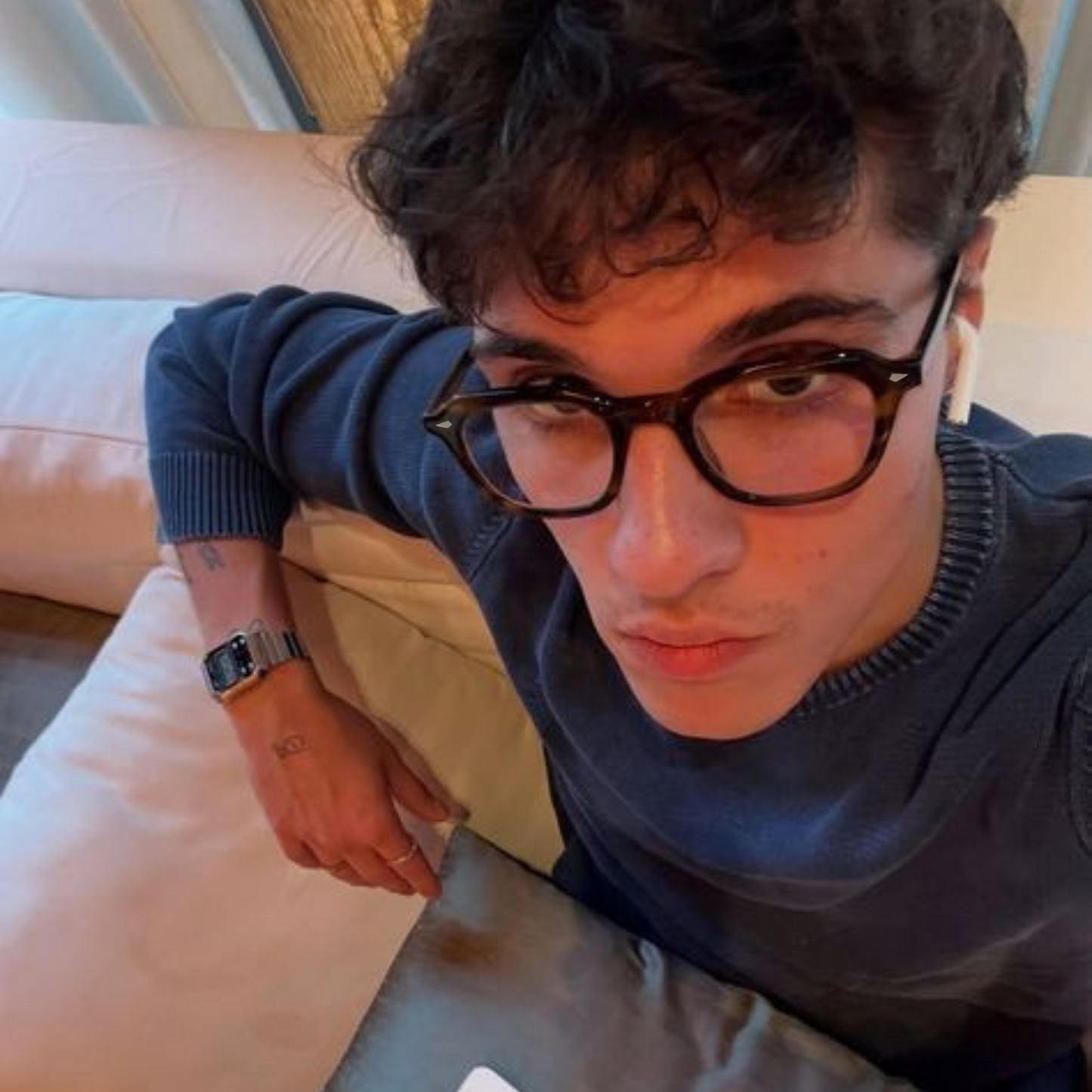 Person wearing glasses and a dark sweater sitting on a couch.